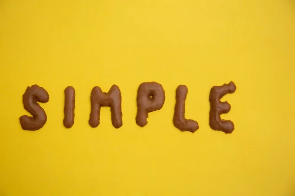 SIMPLE kelime ev yapımı çikolatalı kurabiye alfabesi sarı masa üzerinde düzenlenmiştir