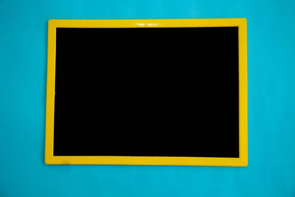 Top view of black chalk board with yellow frame isolated on blue