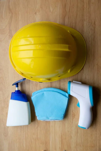 Tıbbi termometre, sarı bir şapka, maskeler ve ahşap bir masada antiseptik el jeli.