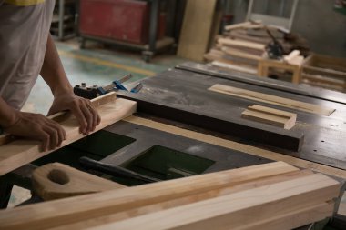 Gri tişörtlü genç bir marangoz, atölyede, arka planda ahşap tahtalarda ve atölyede değirmen makinesi olan ahşap bir bara eşittir.