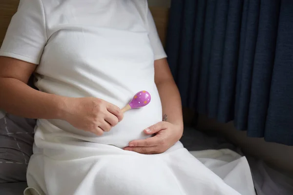 Genç Asyalı Hamile Kadın doğmamış bebeğiyle oynamak için çıngıraklı oyuncak kullanıyor.