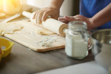 Dişi eller, un serpiştirilmiş ahşap bir masaya mantı ya da mantı yapmak için merdaneyle hamuru yuvarlıyor. Mantı ya da mantı pişirmek için adım adım bir tarif.