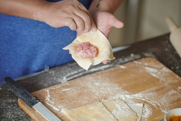 Kadının ellerinin ahşap raptiyeyle etli hamur tatlısı yaptığı ön manzara. Ev yapımı hamur tatlısı yapma süreci. Hamurda kıyma, İtalyan mantısı pişirme süreci. Rus yemeği.