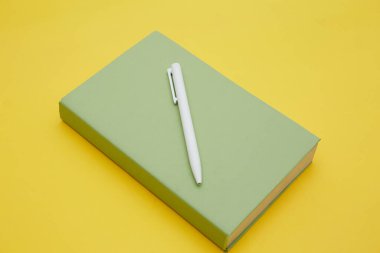 Sarı üzerine izole edilmiş yeşil kitap ve kalemin üst görünümü 