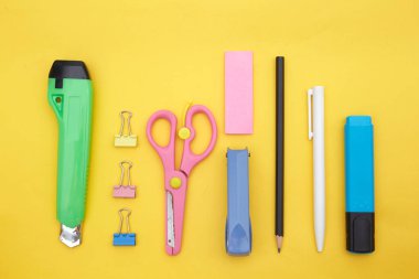 Okul tedarikçilerinin üst görünümü: kağıt bıçağı, ataç, makas, sarı üzerine izole kalem 