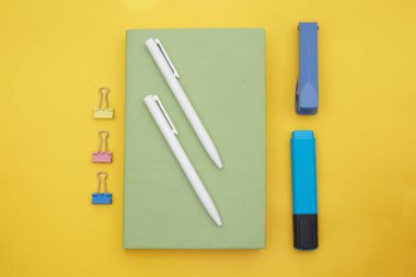 Yeşil kitap, beyaz kalem ve okul tedarikçilerinin sarı arka planda üst görünümü 