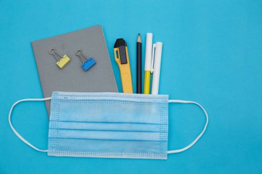 Eğitim seti. Okul. Serbest çalışma, ofis aletleri ve tıbbi maske. Sosyal mesafeyi, uzaktan eğitimi, evde eğitimi, koronavirüsü, karantinayı kavramsallaştırın. Evde kal, güvende kal.