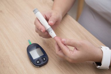 Kan şekeri seviyesini ölçmek için kadın ellerini ilaç, diyabet, glisemi, sağlık ve insanların konseptini kullanarak parmak üzerine mızrak kullanarak Glikoz ölçer kullanarak kapatın.