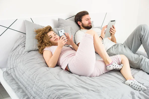 Pár v posteli s tabletu a chytrý telefon — Stock fotografie