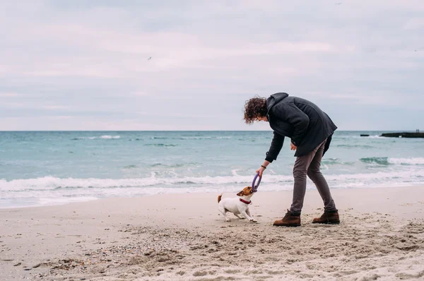Чоловік грає з джек-російським тер'єром на пляжі — стокове фото
