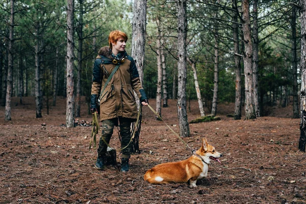 Pelirroja chica caminando con galés corgi perro en el bosque — Foto de Stock