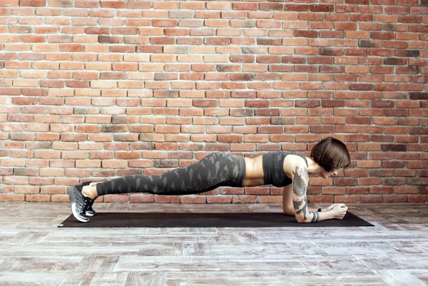 Mujer tatuada haciendo ejercicios en interiores, mujer deportiva practicando yoga — Foto de Stock