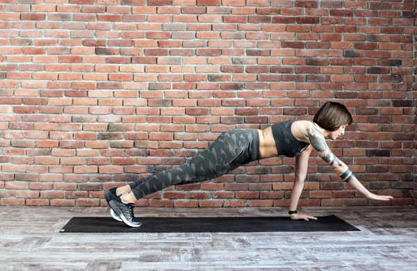 tattooed female doing exercises indoors, sporty woman practicing yoga