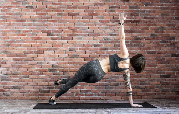 tattooed female doing exercises indoors, sporty woman practicing yoga