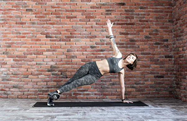 Mujer tatuada haciendo ejercicios en interiores, mujer deportiva practicando yoga — Foto de Stock