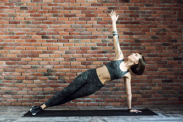 tattooed female doing exercises indoors, sporty woman practicing yoga