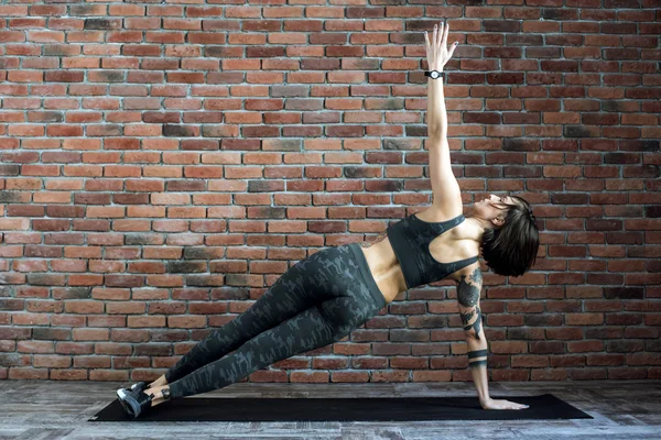 Mujer tatuada haciendo ejercicios en interiores, mujer deportiva practicando yoga — Foto de Stock