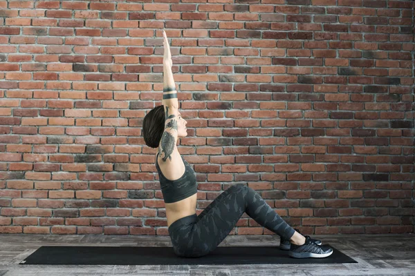 Tattooed female doing exercises indoors, sporty woman practicing yoga — Stock Photo, Image