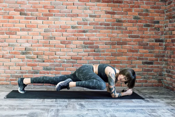 Mujer tatuada haciendo ejercicios en interiores, mujer deportiva practicando yoga — Foto de Stock