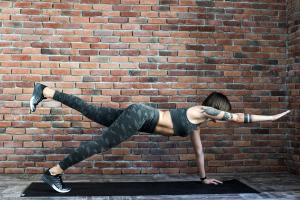 Tatuado feminino fazendo exercícios dentro de casa, mulher esportiva praticando ioga — Fotografia de Stock