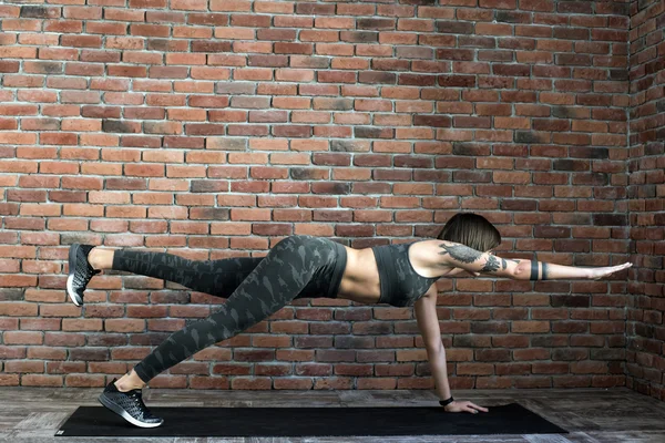 tattooed female doing exercises indoors, sporty woman practicing yoga