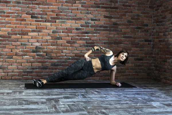 Mujer tatuada haciendo ejercicios en interiores, mujer deportiva practicando yoga — Foto de Stock