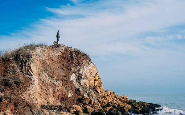 Hombre de pie sobre un acantilado con perro labrador y mirando al mar — Foto de Stock