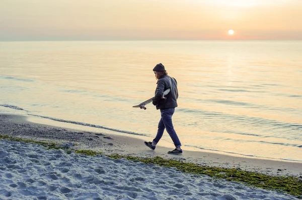 Hombre con patín en la playa al atardecer al amanecer — Foto de Stock