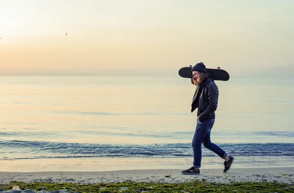 Hombre con patín en la playa al atardecer al amanecer — Foto de Stock