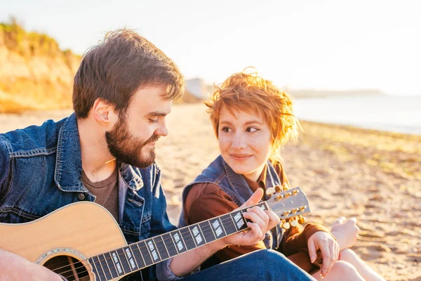 couple playing guitar on beach