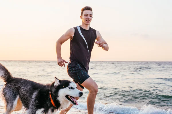 Homem correndo com cão na praia — Fotografia de Stock