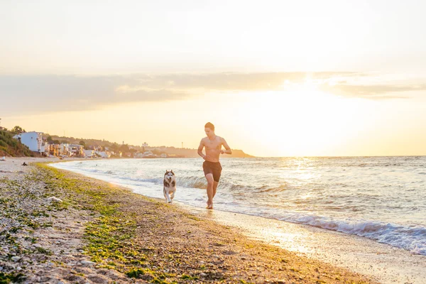 Homem correndo com cão na praia — Fotografia de Stock