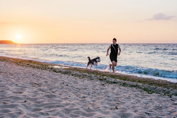 Homem correndo com cão na praia — Fotografia de Stock