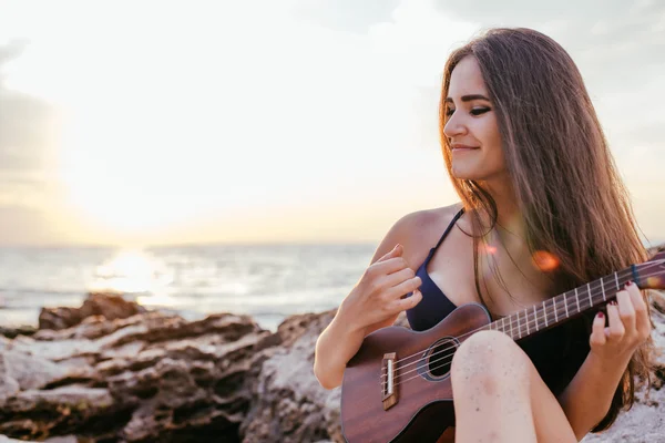 female playing ukulele on beach