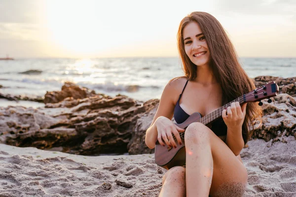 female playing ukulele on beach