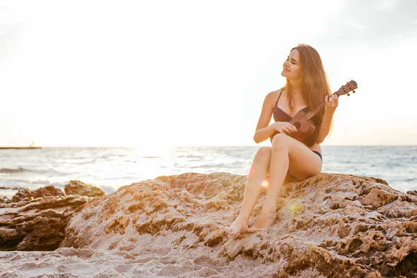 female playing ukulele on beach