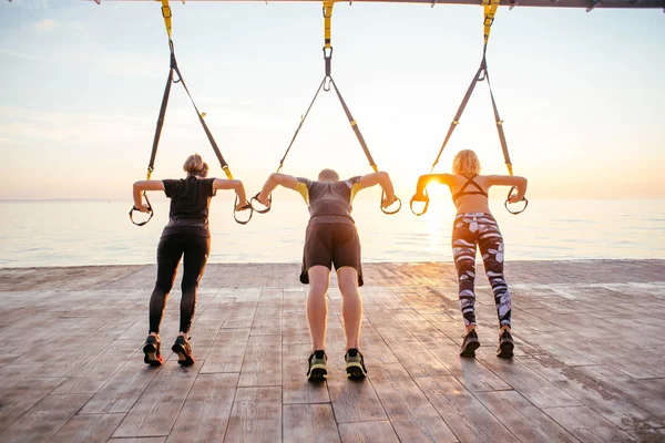 Entrenamiento con correas de suspensión En el gimnasio al aire libre,  fuerte entrenamiento de hombre temprano en la mañana en el parque, amanecer  o atardecer en el fondo del mar: fotografía de