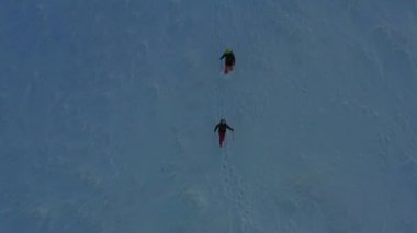 Güzel karlı dağlarda iki yürüyüşçünün 4K hava görüntüsü. İki Sibiryalı köpek kışın dağlarda yürüyüş yapıyor. Uzak yerlere seyahat kavramı