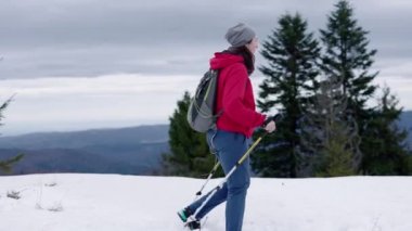 Kırmızı ceketli bir kadın karlı dağlarda doğa yürüyüşü yapıyor. Yürüyüşçü, güzel dağ arka planına karşı. Etkin yaşam tarzı ve uzak yerlere seyahat kavramı