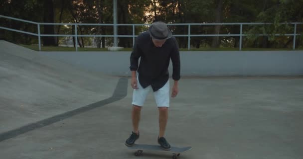 スタイリッシュなミレニアルスケータースケートボードの広い4Kスローモーションショットに続くと彼のスケートボードでトリックを行う屋外スケーターパーク — ストック動画