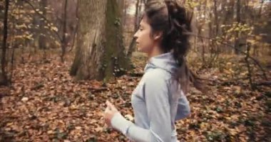 Sonbahar ormanlarında koşan genç bir kadın. Soğuk havada dışarıda egzersiz yapmak.