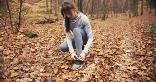 秋天的森林里 年轻的女运动员正在系鞋带 寒冷天气下户外活动 — 图库视频影像