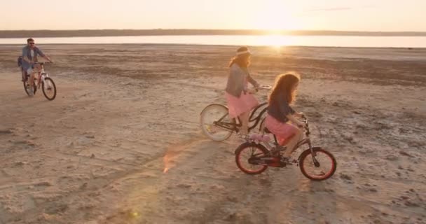 一家四口 女儿和小儿子在美丽的夕阳西下骑自行车来到湖边 暑假的概念 — 图库视频影像