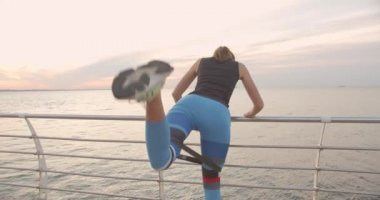 Gün batımında ya da gün doğumunda deniz kenarında egzersiz yapan genç bir kadın. Sağlıklı yaşam tarzı ve spor anlayışı