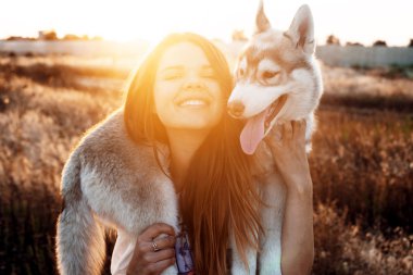 gün batımı sırasında Sibirya husky köpek alanında oynamaktan genç beyaz kadın. Having oyunculuk köpek yavrusu ile açık havada güzel ışıkta mutlu gülümseyen kız