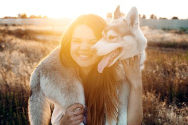 gün batımı sırasında Sibirya husky köpek alanında oynamaktan genç beyaz kadın. Having oyunculuk köpek yavrusu ile açık havada güzel ışıkta mutlu gülümseyen kız