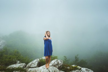 sisli hava dağlarında mavi elbiseli poz genç beyaz kadın