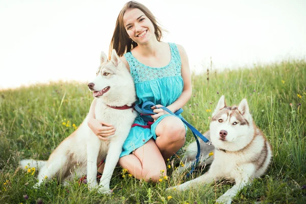 หญิงสาวผิวขาวที่มีสุนัขฮัสกี้ไซบีเรียสองตัวนั่งอยู่บนสนามในภูเขาอาชญากรรม — ภาพถ่ายสต็อก