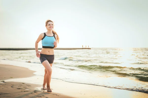 Systemem kobieta. Kobiece kobieta lekkoatletka joggingu podczas słońca na plaży. — Zdjęcie stockowe