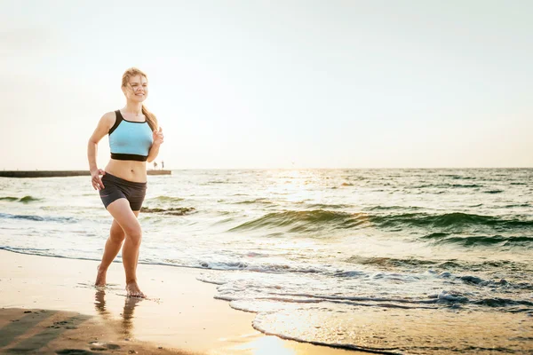 Systemem kobieta. Kobiece kobieta lekkoatletka joggingu podczas słońca na plaży. — Zdjęcie stockowe